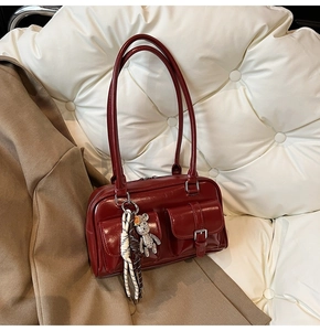 Close-up of deep red glossy shoulder bag featuring front pockets and rhinestone bear charm