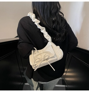 Detail of white glossy leather shoulder bag with bow and ruffled cloud strap