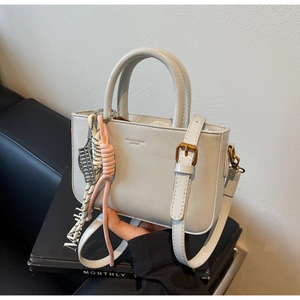 Close-up of gray leather handbag with MAQUIE & BAGS embossed logo and decorative charm