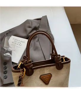 Detail of beige canvas tote with brown leather trim and triangle metal logo plaque