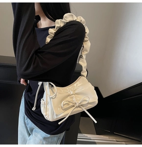 Detail of cream white shoulder bag with large bow design and ruffled strap on a model