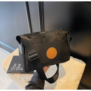 Gros plan d'un sac bandoulière en nylon noir avec logo en cuir marron sur plateau en pierre