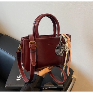 Close-up of deep burgundy glossy mini bag with tennis racket charm and woven cord detail