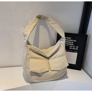 Detail of beige quilted puffer tote bag featuring two front pockets and wide shoulder strap