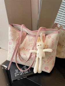 Large beige tote bag with pink graffiti prints and a cute rabbit pendant on a black book