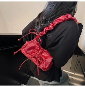 Close-up of a red patent leather shoulder bag with bow knot and pleated cloud strap