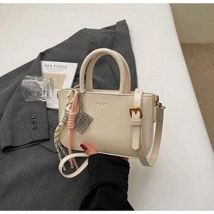 Detail of cream crossbody bag with leather texture, logo print, and tennis racket charm