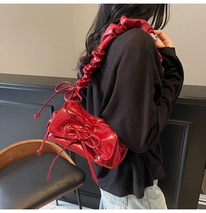 Detail view of red pleated underarm bag with glossy patent leather and bow accents