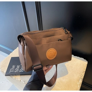 Détail de la bandoulière large et des poches zippées du sac en nylon marron pratique