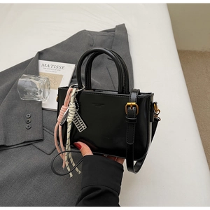 Close-up of black patent leather handbag with decorative tassel and silver abacus pendant