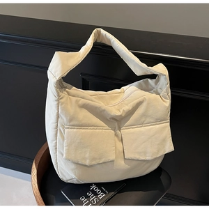 Detail of beige quilted tote bag featuring two front patch pockets and zip closure