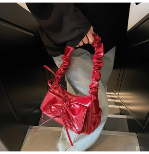 Detail of red patent leather handbag featuring pleated handle and bow decoration