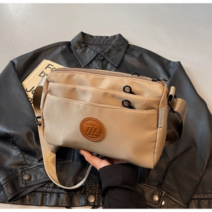 Détail d'un sac bandoulière en nylon kaki avec trois compartiments zippés et logo