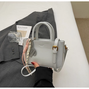 Detail of light gray crossbody bag with vintage gold hardware and creative charms