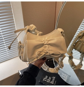 Close-up of cream bow bag with ruched handle held against an aesthetic background