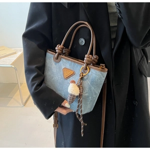 Detail of light blue denim tote with brown leather handles and a plush ice cream charm