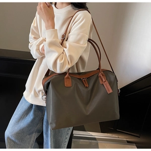 Detail of olive green nylon tote bag with brown leather handles and side tag for travel