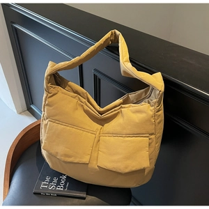 Close-up of a quilted puffer tote bag in yellow with dual front pockets on a black chair