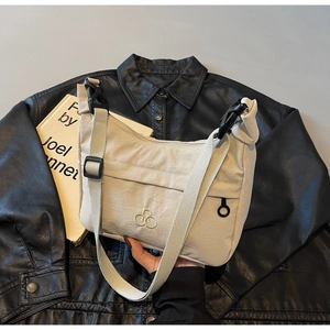 Dettaglio borsa a tracolla beige con logo in metallo e fibbie regolabili su giacca nera