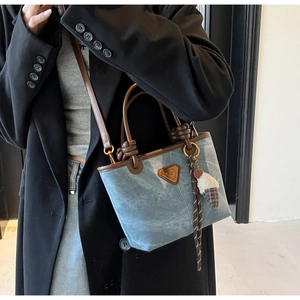 Detail of blue denim tote bag with brown leather handles and plush charm accessory