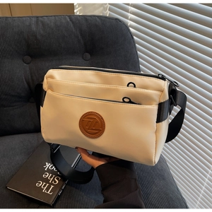 Détail de la sacoche en nylon blanc cassé avec zips multicouches et écusson en cuir brun