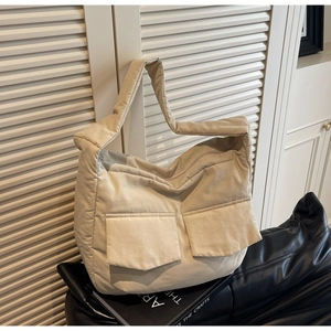 Detail of beige quilted tote bag featuring two front flap pockets and plush padded fabric