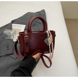 Macro view of burgundy PU leather handbag with side charm on a grey suit jacket