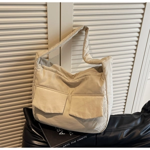 Detail view of a beige quilted tote bag with dual front pockets and wide shoulder strap