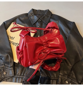 Detailed shot of bright red patent leather bow handbag with pleated handle on jacket
