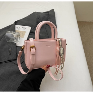 Detail of light pink leather handbag with braided rope charm on a grey blazer