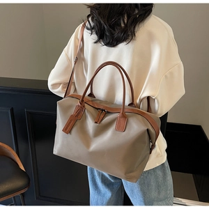 Large taupe nylon tote bag with brown leather handles worn by a model in a room