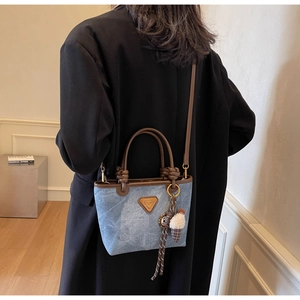 Detail of denim bucket bag with brown leather trim and decorative bag charms