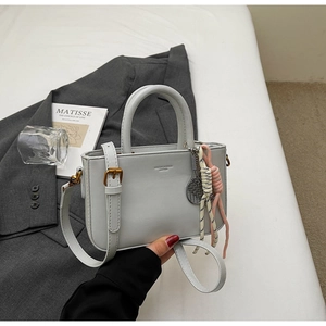 Detail of light gray leather bag with gold logo, bronze hardware and tennis racket charm