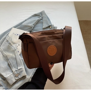 Détail du sac bandoulière en nylon marron chocolat avec logo sur veste en jean