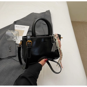 Detail of black glossy handbag with woven cord pendant and silver metal charm accessory