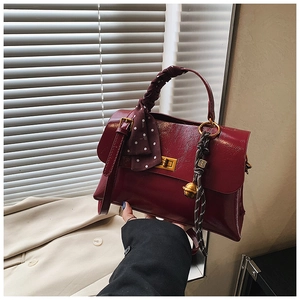 Close-up of burgundy leather handbag featuring a gold twist lock and silk scarf handle detail
