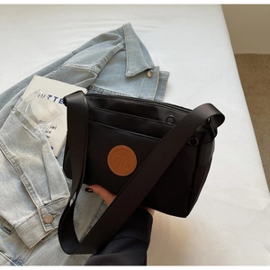 Détail du sac bandoulière en nylon noir avec fermetures éclair et logo en cuir