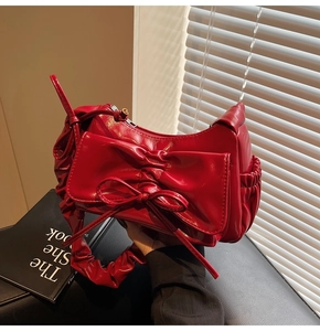 Detail of red pleated shoulder bag featuring a large decorative bow and glossy finish