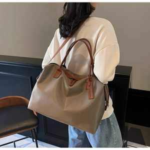 Detail of khaki nylon tote bag with brown leather handles and side brand tag on model