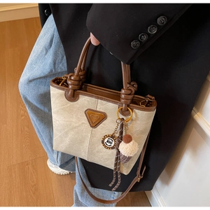 Detail of beige canvas bucket bag with brown leather trim and ice cream charm