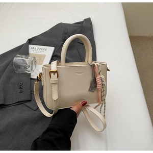 Detail of off-white rectangle handbag with gold hardware and tennis racket bag charm accessory