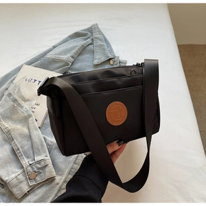 Gros plan d'un sac bandoulière noir en nylon avec fermetures éclair et logo rond en cuir