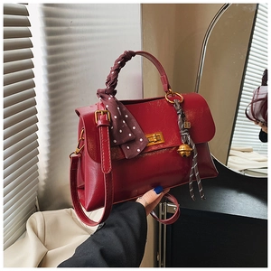 Detail of red leather handbag with gold twist lock, silk scarf handle, and tassel charm