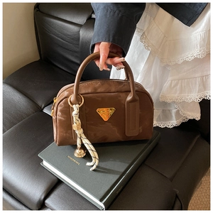 Détail du sac bowling marron foncé avec plaque logo dorée et pendentif tressé élégant