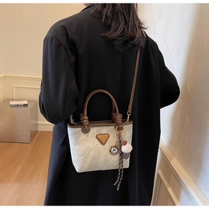 Detail of canvas tote bag with braided handle and cute charms shown on crossbody model