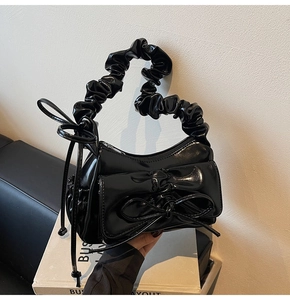 Detail of glossy patent leather shoulder bag with ruffled handle and bow decoration