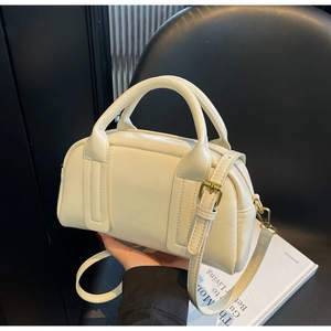 Gros plan du sac Boston crème avec texture cuir fin et détails en métal doré mat
