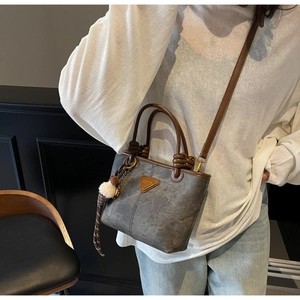 Detail of dark grey retro bucket bag with knot handle and plush ball charm accessory
