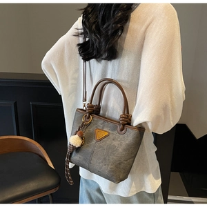 Detail of grey crossbody bucket bag with brown leather handles and bear pendant decor