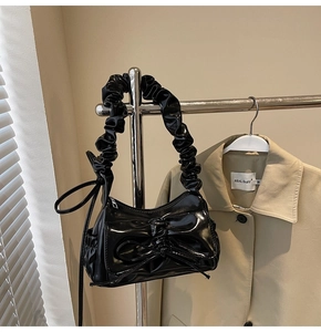 Detail of black glossy bow shoulder bag with pleated handle on a metallic stand